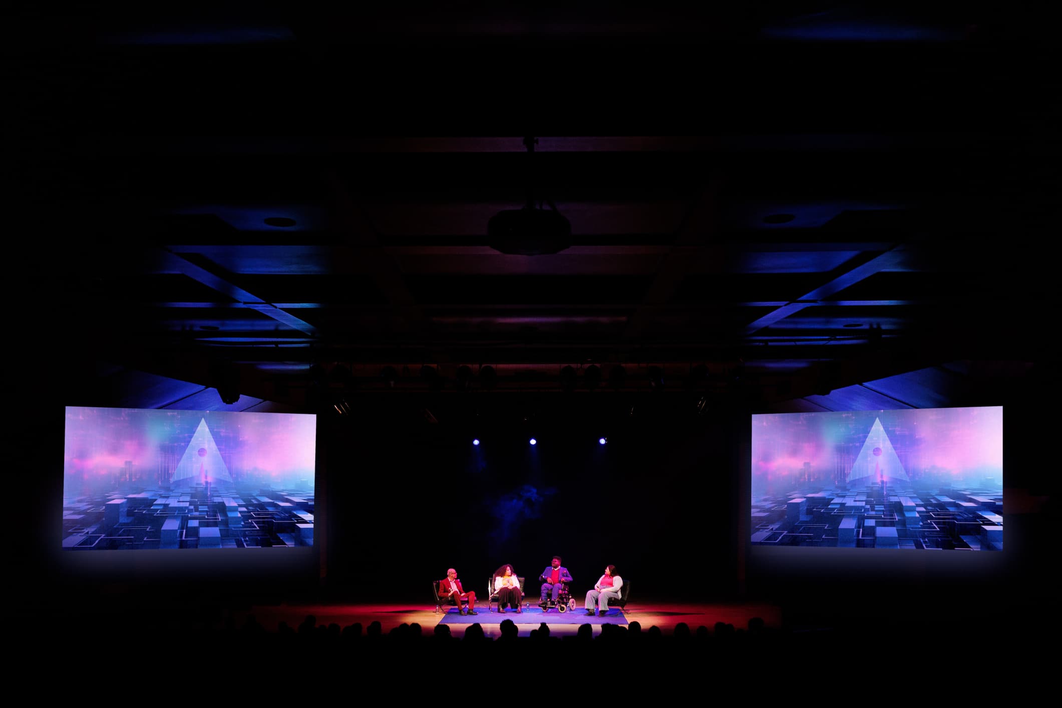 Conference panel discussion on stage with four speakers under dramatic lighting